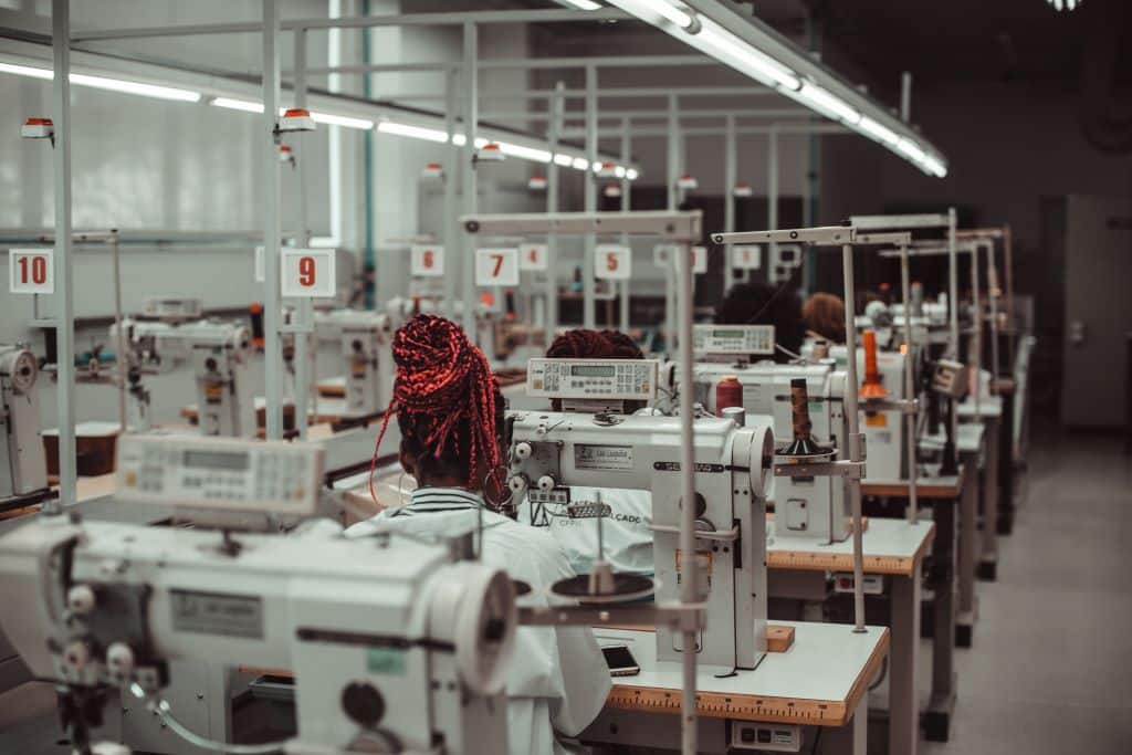 Pessoas em atividade laboral que consiste no trabalho com máquinas de costura.